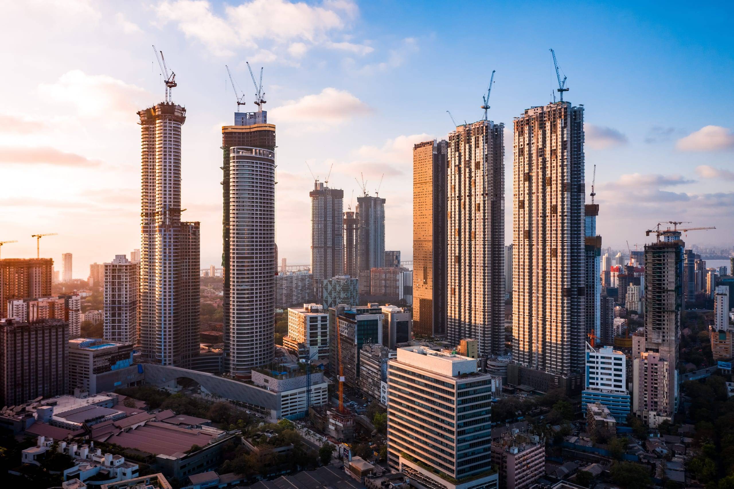 Golden-hour aerial of the Mumbai skyline, with residential towers under construction and tower cranes across the district.