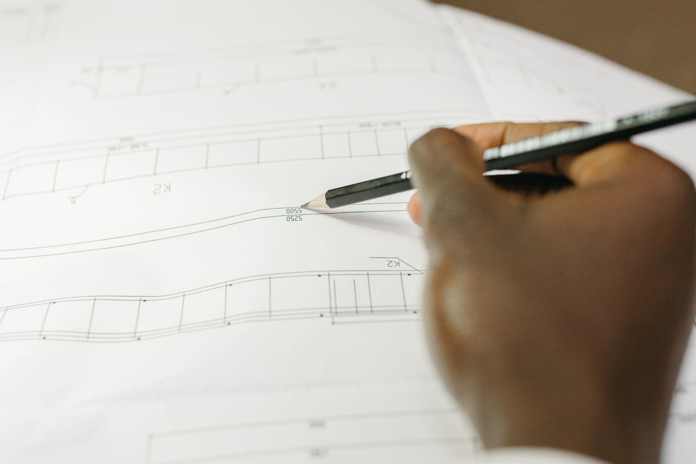 A hand marking a contour line on an engineering drawing.