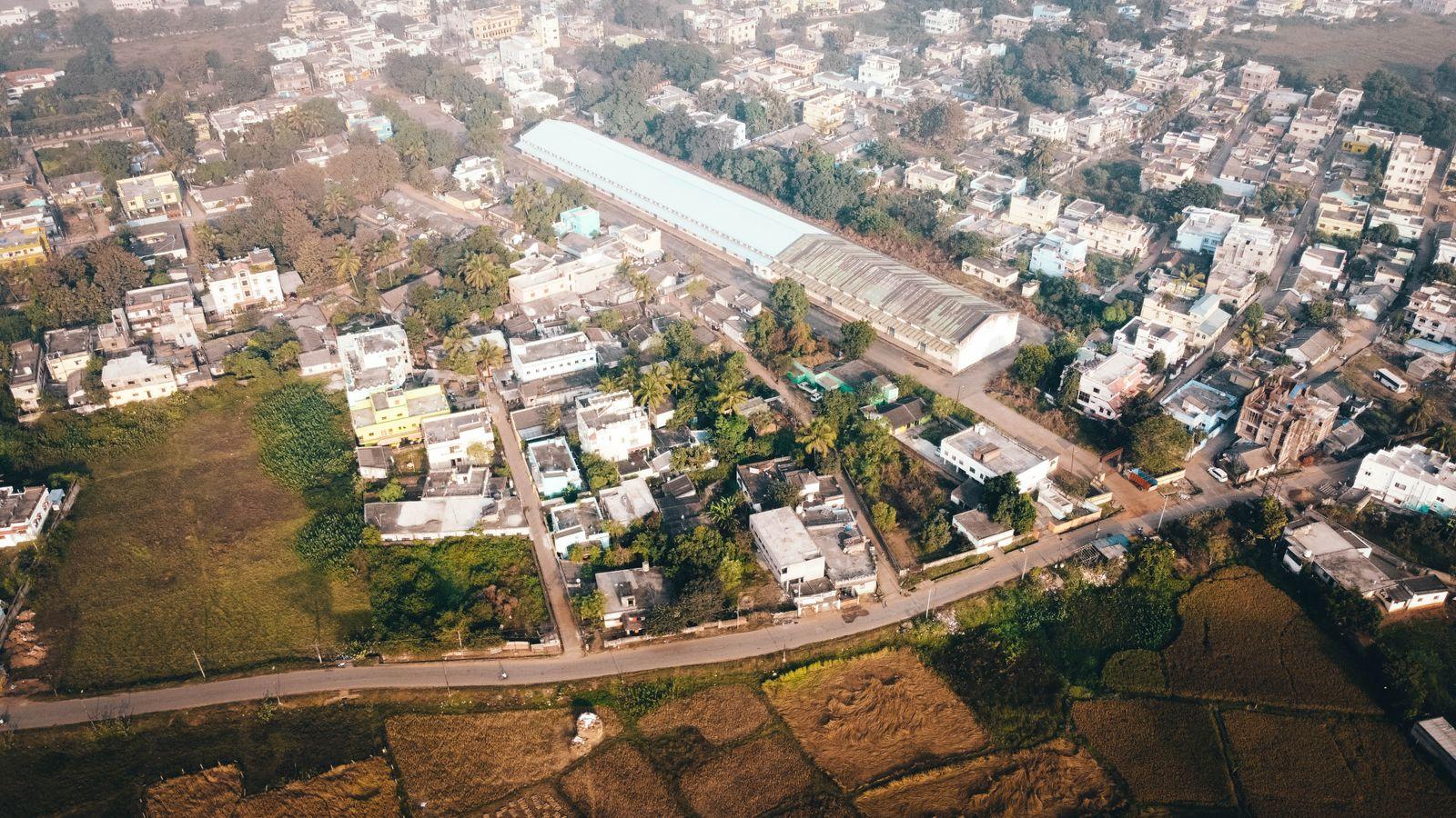 An aerial view of a town with a long warehouse shed among houses and fields.