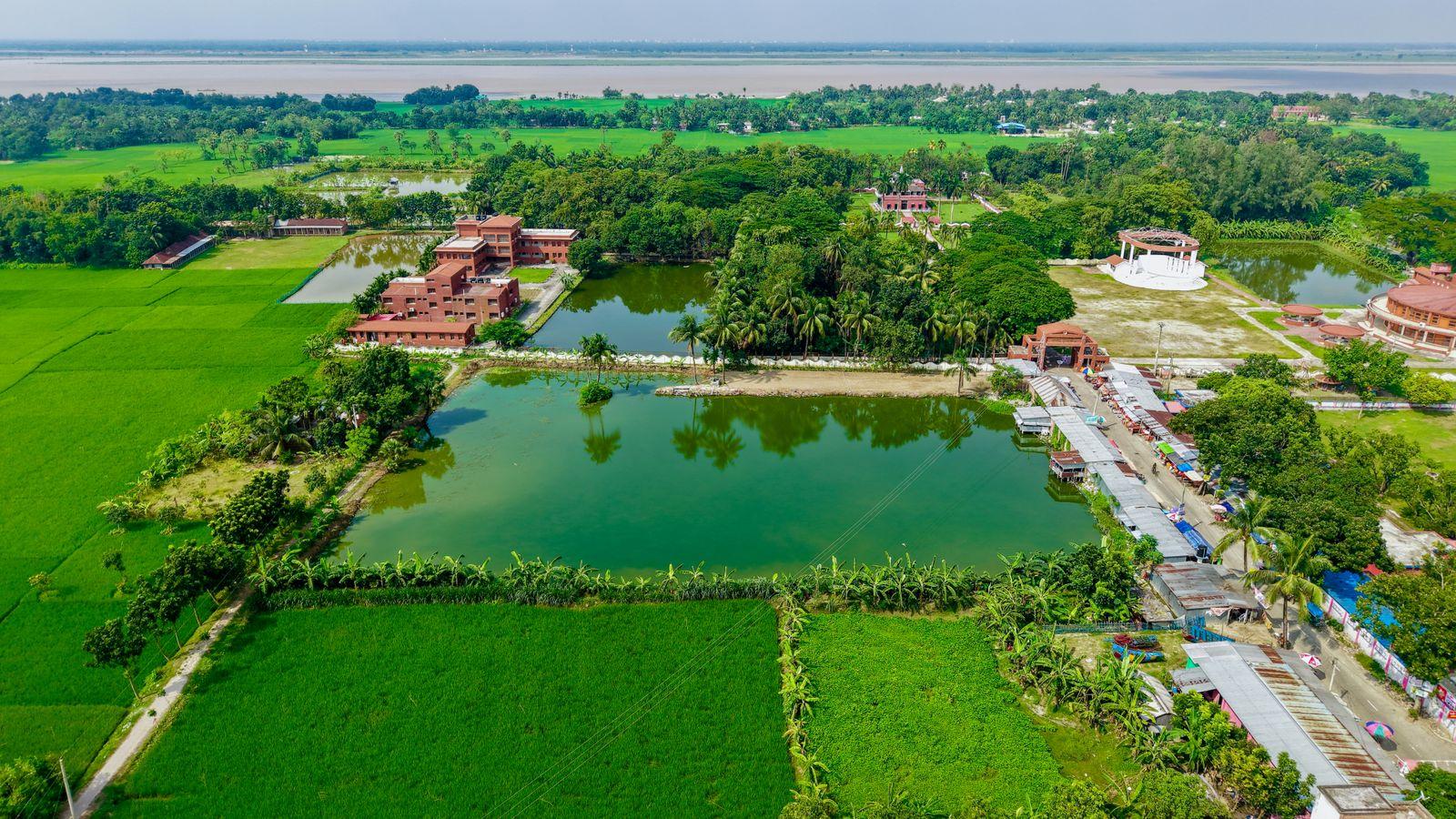 An aerial view of paddy fields, ponds and a village beside a river.