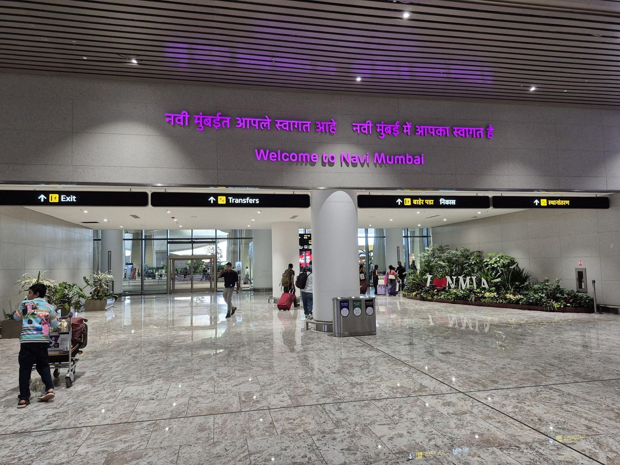 The arrivals hall of Navi Mumbai International Airport with a Welcome to Navi Mumbai sign.