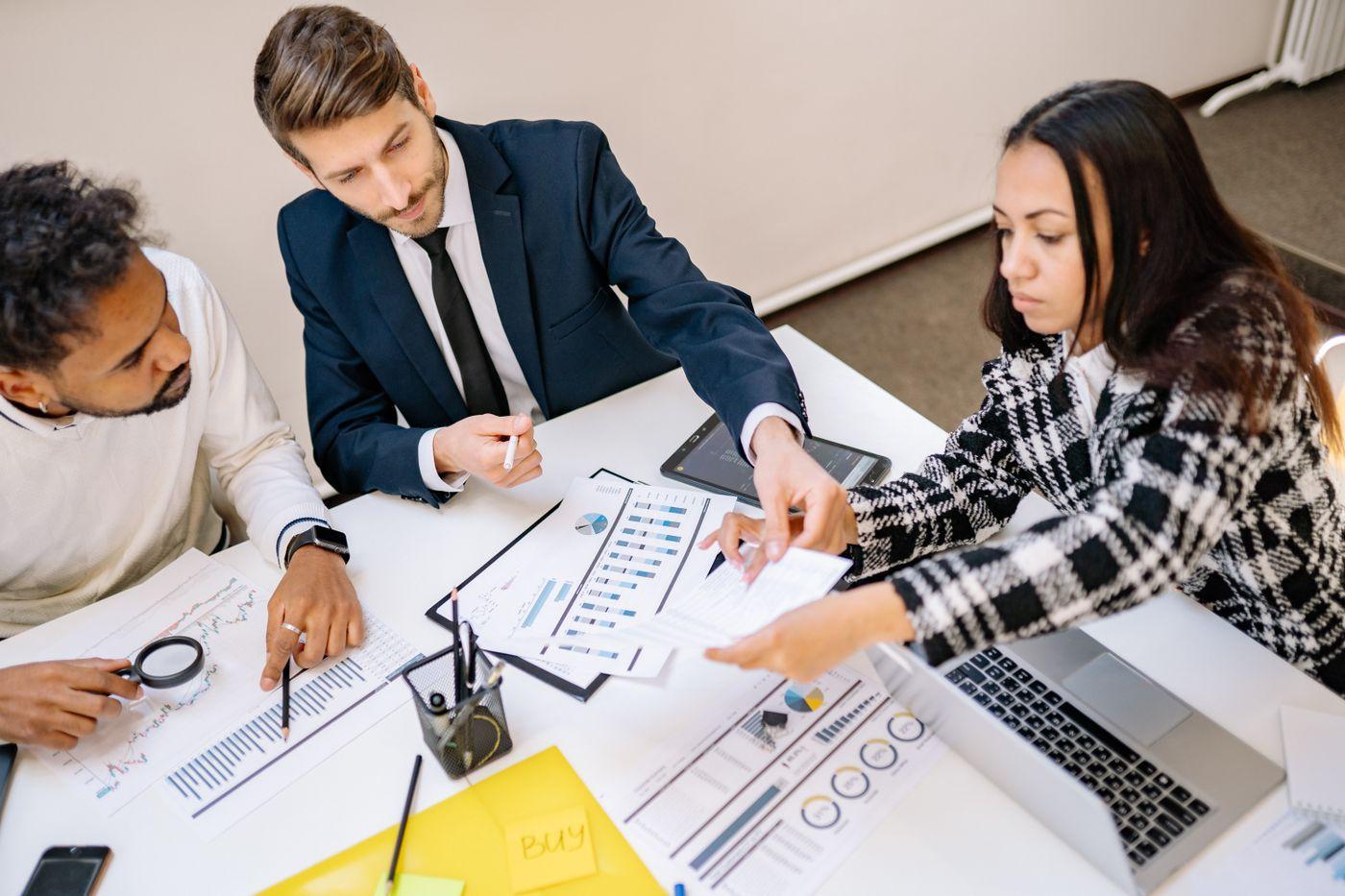 Three colleagues comparing printed charts and figures at a desk.