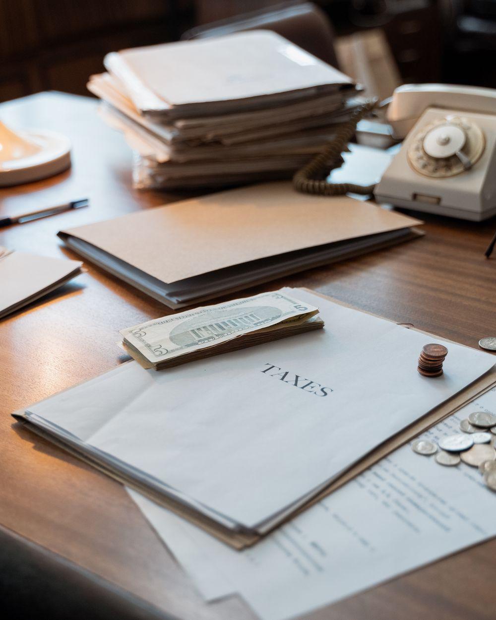 A folder marked Taxes on a desk with banknotes, coins and a rotary telephone.