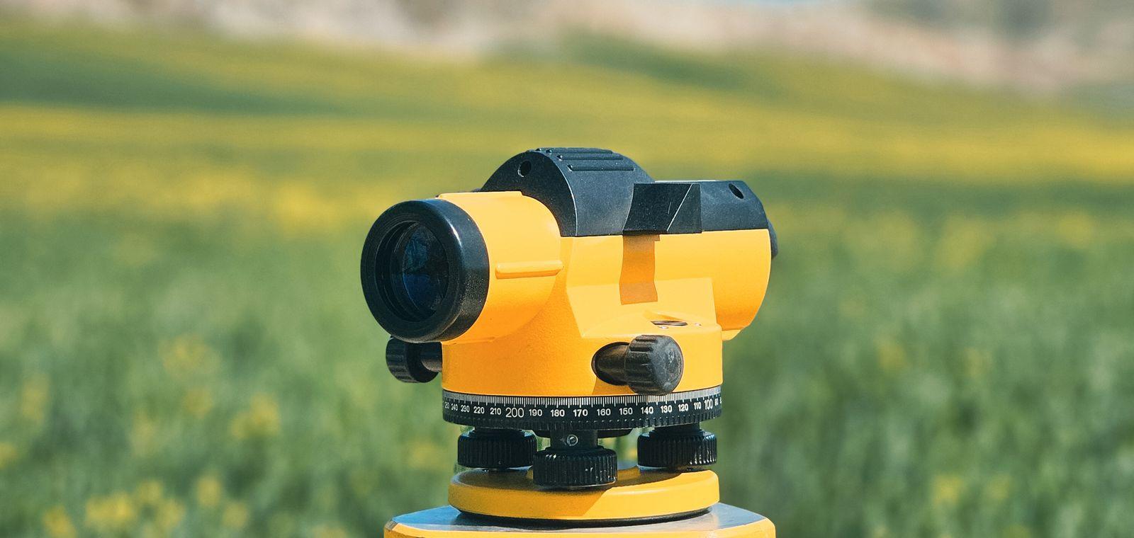 A surveyor's optical level on a tripod in an open field.