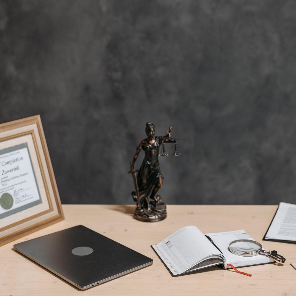 A framed certificate, a figure of Justice and an open ledger on a desk.