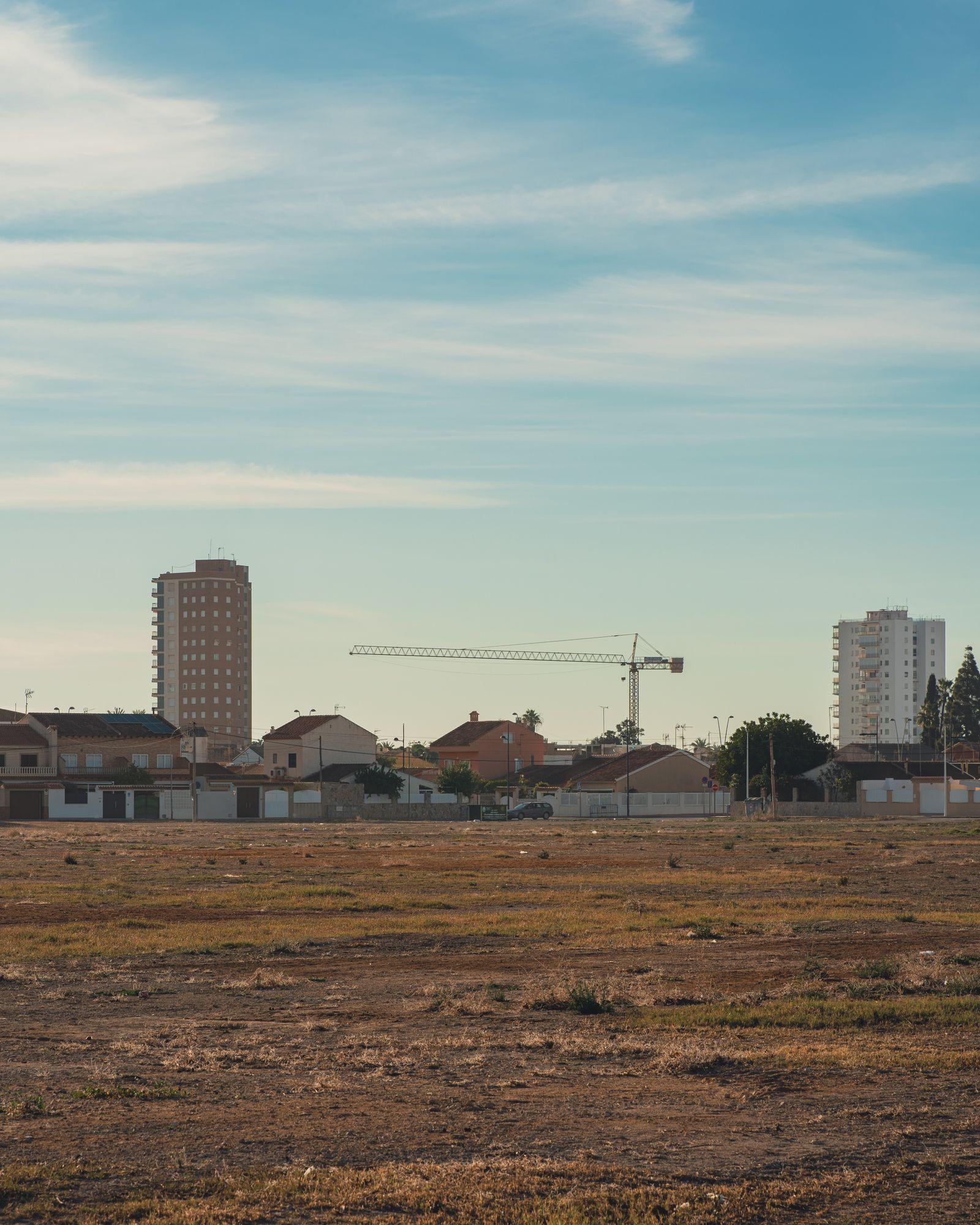 A vacant plot in the foreground with apartment blocks and a tower crane beyond.