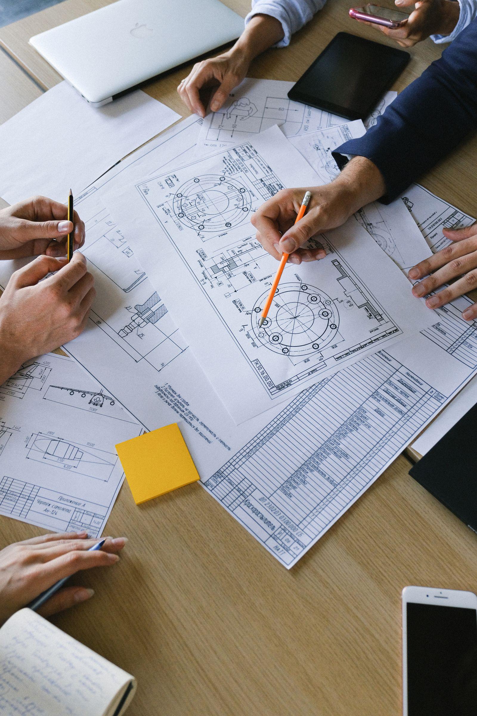 Hands around a table marking up technical drawings.