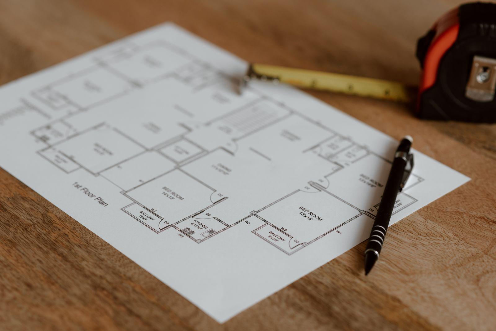 A first-floor plan drawing on a desk with a tape measure and pen.